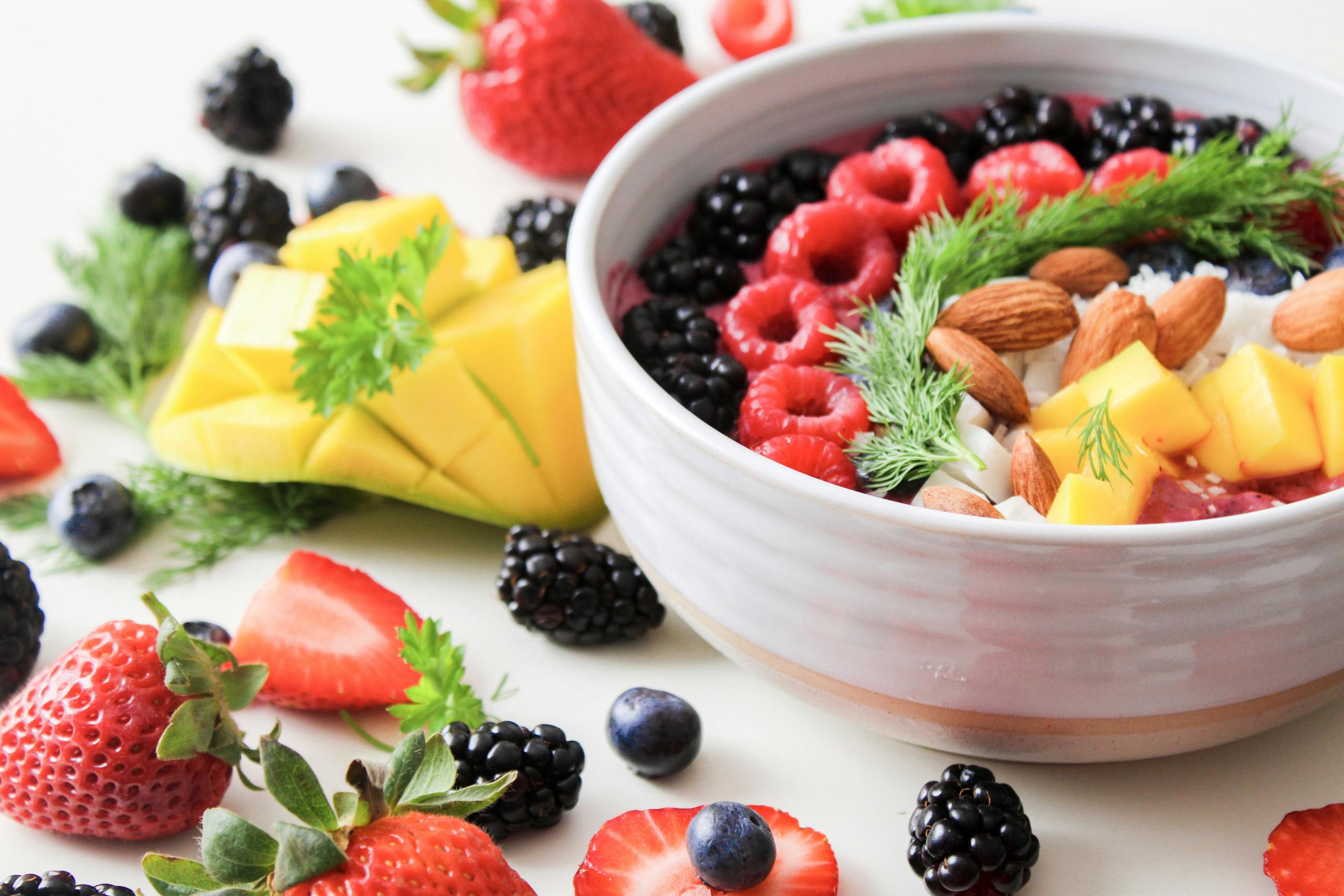 A vibrant bowl filled with fresh berries, mango, almonds, and herbs, perfect for a healthy snack or breakfast.