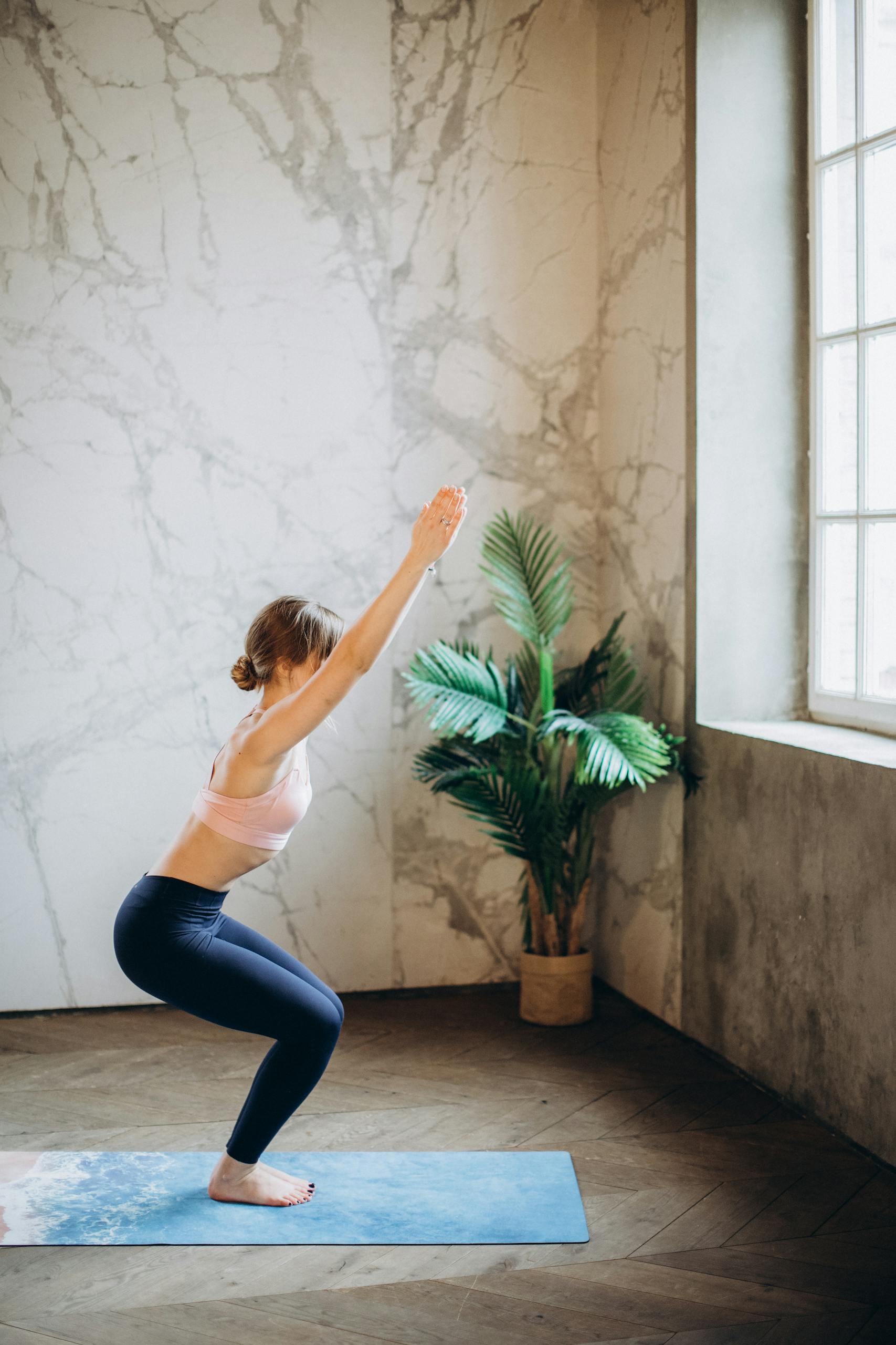 Adult woman performing yoga indoors with window light, enhancing relaxation and mindfulness.